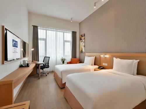成都市にあるHoliday Inn Express Chengdu Huanhuaxi, an IHG Hotelのベッド2台とデスクが備わるホテルルームです。