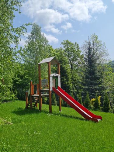 - une aire de jeux avec toboggan rouge dans l'herbe dans l'établissement Apartament Sun House 60 z prywatną SAUNĄ KOMINKIEM i widokiem na SKRZYCZNE, à Szczyrk