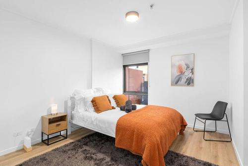2-Bedroom Apartment in Paris End of Melbourne CBD في ملبورن: غرفة نوم بسرير وبطانية برتقالية وكرسي