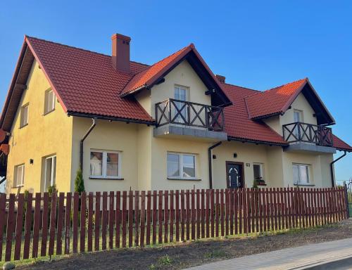 a yellow house with a red roof behind a fence at DOM POD WIŚNIĄ in Giżycko