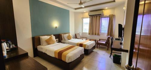 a hotel room with two beds and a desk at Hotel Kanak in Ahmedabad
