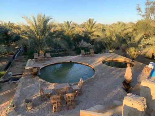 een buitenzwembad met stoelen, tafels en palmbomen bij Al Kahina Gardens, Retreat and Resort in Siwa