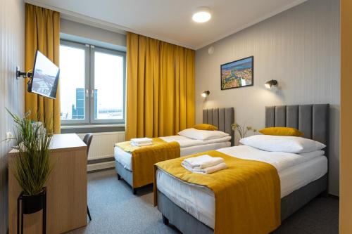 two beds in a hotel room with yellow curtains at Apartamenty Albatros in Augustów