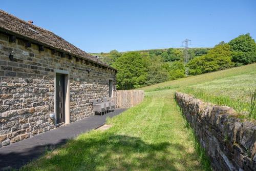 a stone building with two benches next to a wall at Meadow Barn in Rishworth