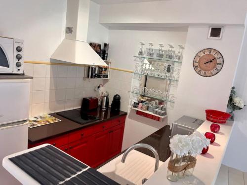 une cuisine avec des placards rouges et une horloge murale dans l'établissement Joli studio tout confort proche toutes commodités, à LʼÎle-Rousse