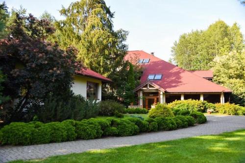uma casa com um telhado vermelho e alguns arbustos em Bobrowy Resort em Zabłudów
