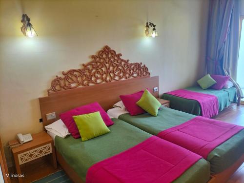 two beds in a room with pink and green at Hôtel LES MIMOSAS TABARKA in Tabarka