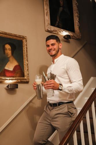 a man standing on the stairs holding a drink and a glass at Henrys Townhouse Marylebone, London in London