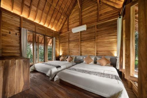two beds in a room with wooden walls and windows at Cay's House Batukaras in Batukaras