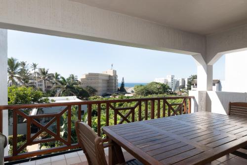 a balcony with a wooden table and chairs and the ocean at La Pirogue 19 in Ballito