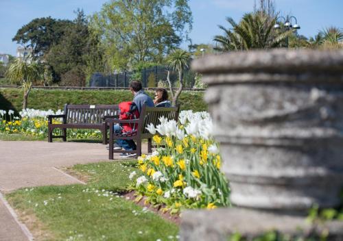 two people sitting on a bench in a park with flowers at Sunnyhill Mews in Torquay