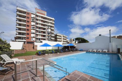 馬德普拉塔的住宿－馬德普拉塔索拉納斯海灘公寓式酒店，一座带椅子和遮阳伞的游泳池位于一座建筑旁边