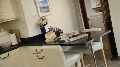 a kitchen counter with white chairs and a black counter top at Holly Tree Lodge in Nicholaston