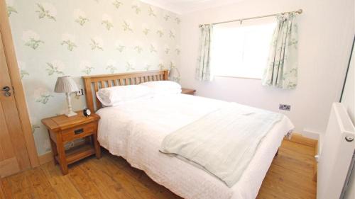 um quarto com uma cama com lençóis brancos e uma janela em Coastal View em Oxwich