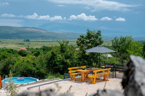 a wooden table and benches with an umbrella and a pool at Sweet Cottage in Mostar