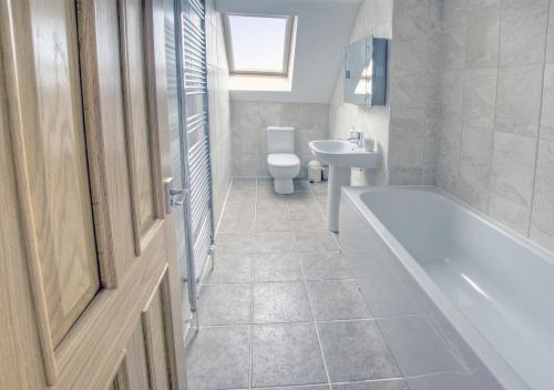 a bathroom with a tub and a toilet and a sink at Holly Cottage in Seaton