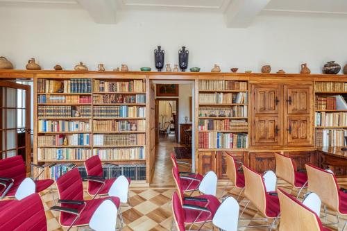 a library with red chairs and wooden bookshelves at Villa by @ Home Hotel Locarno in Locarno