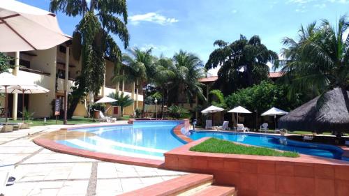 a swimming pool at a resort with palm trees and umbrellas at Solar Pipa Praia Flats in Pipa