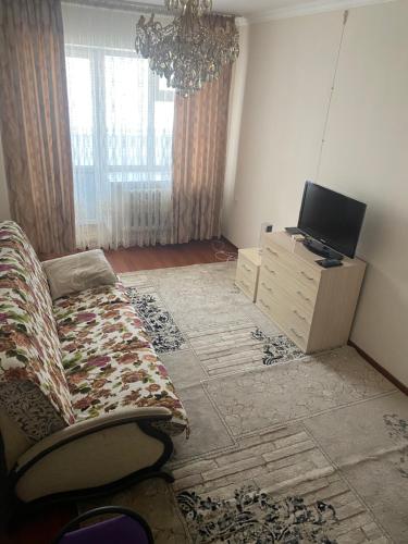 een woonkamer met een bank en een televisie bij Уютная 2-х комнатная квартира in Qizilorda