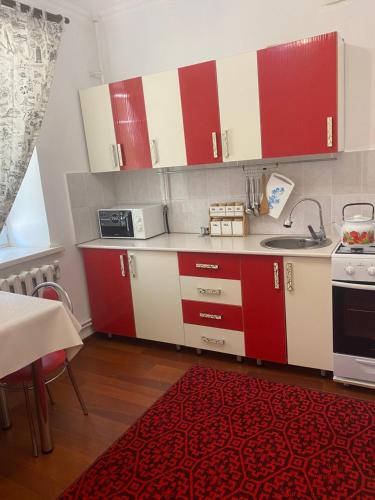 a kitchen with red and white cabinets and a red rug at Уютная 2-х комнатная квартира in Qyzylorda