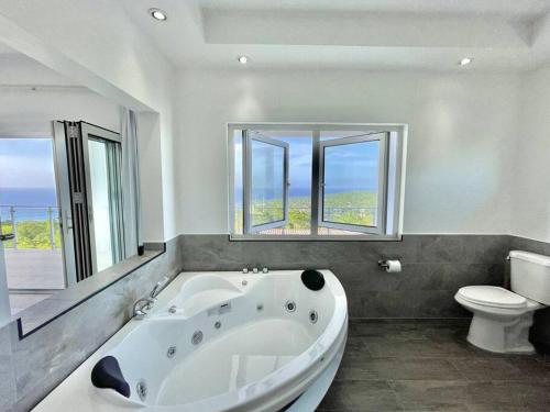 ein Badezimmer mit einer großen weißen Badewanne und einem WC in der Unterkunft Olive Branch Villa *Luxury/ Fine Dining* in Oracabessa