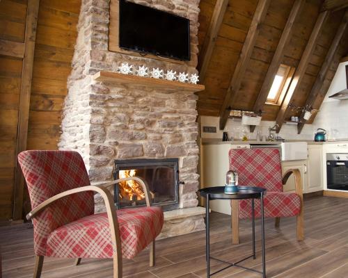 a living room with a stone fireplace with two chairs and a table at Yaban Yasam Chalets in Yolcatı