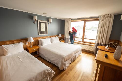 a hotel room with two beds and a woman looking out the window at Hotel Bellavista in Puerto Varas