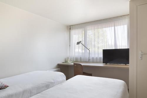 a room with two beds and a desk with a television at Campanile Dole in Dole