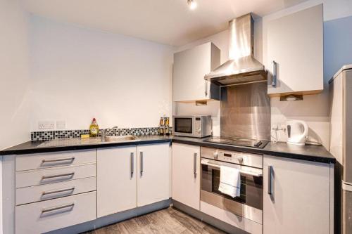 een keuken met witte kasten en roestvrijstalen apparatuur bij 2 Bed apartment with balcony private parking near Etihad Stadium, COOP Live in Manchester