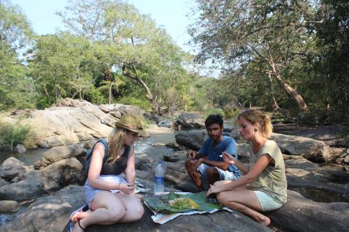 a group of three people sitting on rocks by a river at Kataragama Homestay in Kataragama