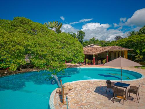 a pool with a table and chairs and an umbrella at Estação Santa Fé Hotel e Pousada in Arraial d'Ajuda
