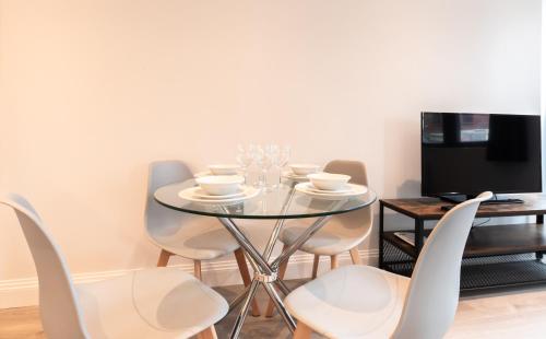 une salle à manger avec une table en verre et des chaises blanches dans l'établissement Kingsbridge House Apartment Four - Free Parking - Heathrow - Thorpe Park, à Staines