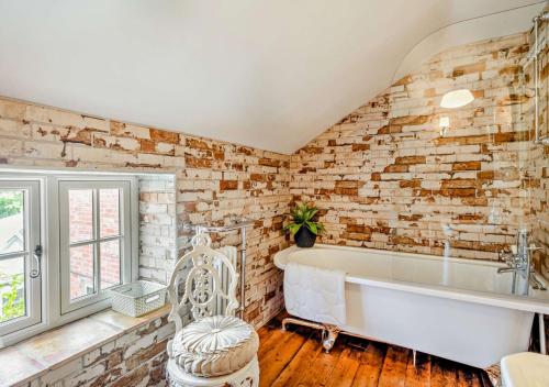 a bathroom with a white tub and a brick wall at Rose Cottage - Sedgeford in Sedgeford