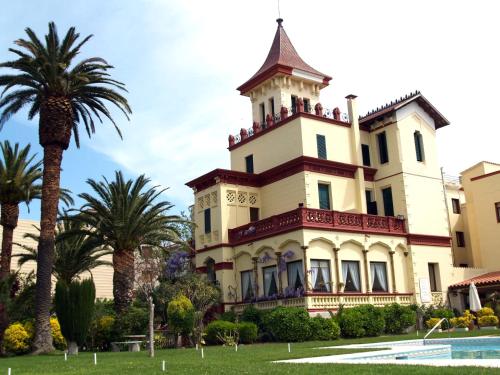 una casa grande con palmeras delante en Hotel Hostal del Sol, en Sant Feliu de Guíxols