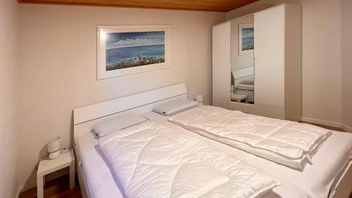 ein weißes Bett in einem Schlafzimmer mit einem Spiegel in der Unterkunft Ferienwohnung am Sonnenstrahl in Dorum Neufeld