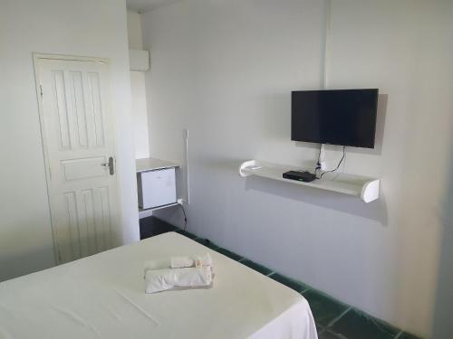 um quarto branco com uma cama e uma televisão na parede em Quintal da Praia em Prado