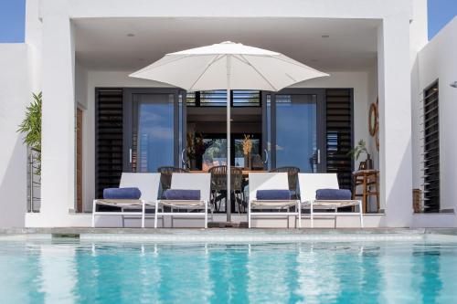 a group of chairs and an umbrella next to a swimming pool at Villa Bon Vista Cas Grandi in Willemstad