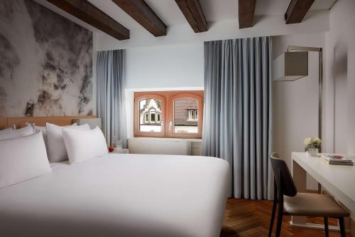 een slaapkamer met een wit bed, een bureau en een raam bij NH Collection Heidelberg in Heidelberg