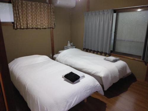 two beds with white sheets in a room with a window at ゲストハウスみちしお in Hikino