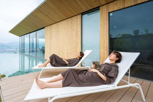 two women sitting in chairs on a balcony with a view of the water at Garden Terrace Nagasaki Hotels & Resorts in Nagasaki
