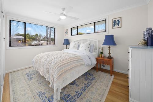 a bedroom with a white bed and two windows at Little Palm Cabins in Lake Cathie