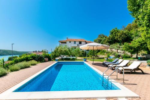 a swimming pool with chairs and an umbrella next to a house at Apartments Zeljko in Kampor