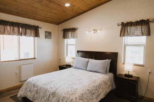 a bedroom with a bed with white sheets and windows at Log Cottages at Bryce Canyon #1 in Cannonville