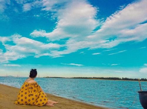 a woman in a yellow dress sitting on the beach at Hùng Đức Hotel Cửa Lò in Cửa Lô