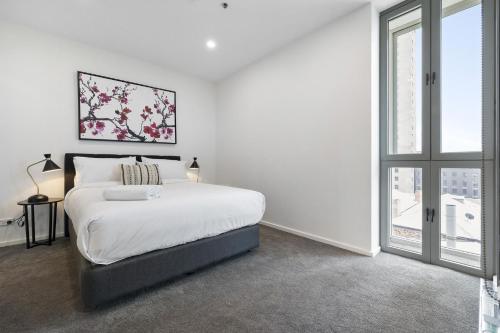 a white bedroom with a bed and a window at Meadow - The York Skyline Apartment in Adelaide