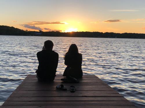 Un hombre y una mujer sentados en un muelle mirando la puesta de sol en Lakefront Cabin Pvt Beach and Dock - Sunset Marina, en Arrowhead Lake