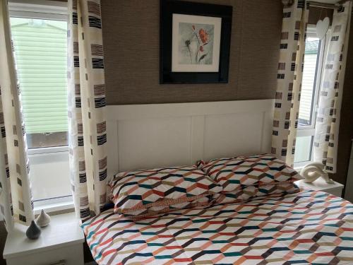 um quarto com uma cama com um edredão e 2 janelas em Luxury Caravan - WI-FI and SMART TV newly installed em Rhyl