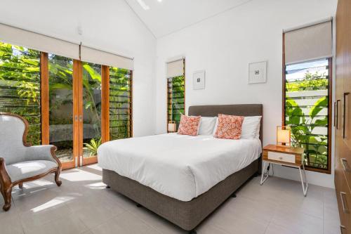 a bedroom with a bed and a chair and windows at Belle Escapes Luxury Reef Villa Palm Cove in Palm Cove