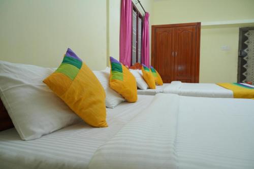 a row of white beds with colorful pillows on them at Umaiyyal Home Stay in Kanyakumari