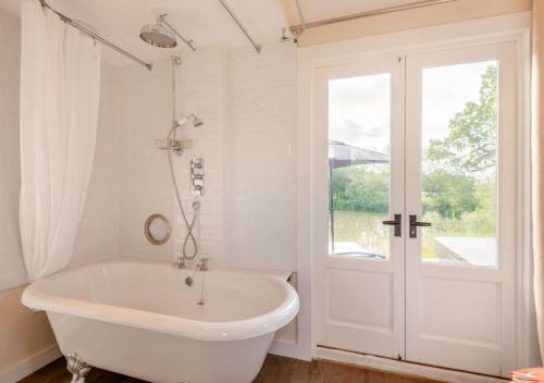 baño con bañera blanca y ventana en The Boathouse, en Biddenden
